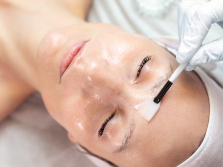 Gros plan sur un chirurgien esthétique en train d'appliquer un peeling au phénol sur une jeune cliente dans une clinique de chirurgie esthétique.