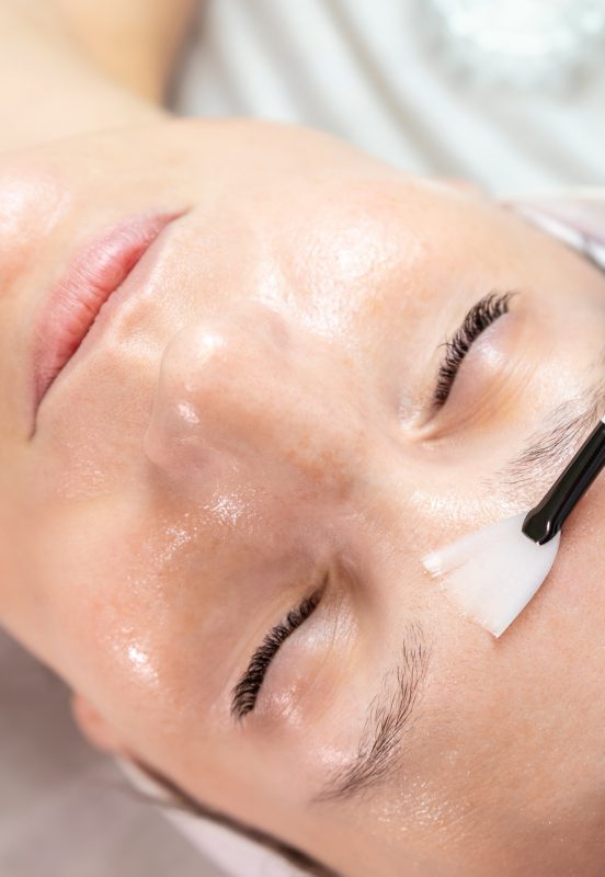 Gros plan sur un chirurgien esthétique en train d'appliquer un peeling au phénol sur une jeune cliente dans une clinique de chirurgie esthétique.