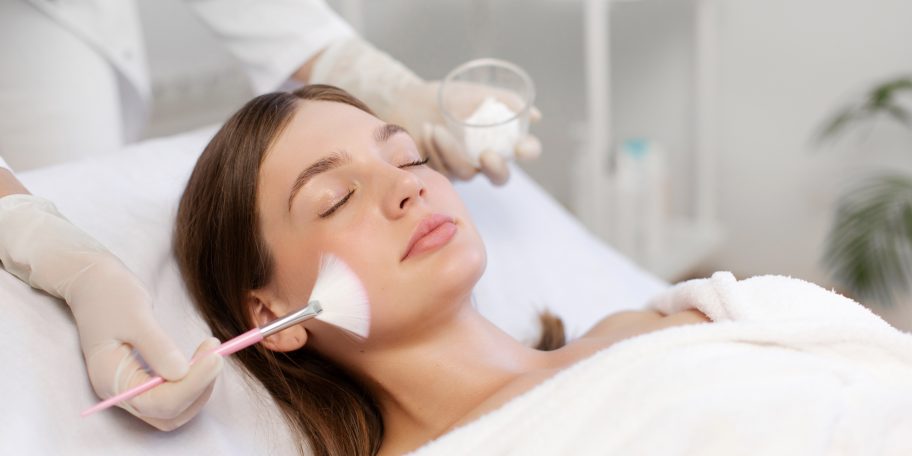 Une femme bénéficie d'un soin du visage professionnel allongée sur une table; le chirurgien esthétique lui applique un peeling sur le visage